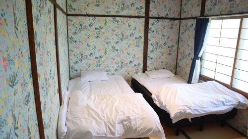 two twin beds in a room with floral wallpaper at 東神楽大学ゲストハウス in Higashikagura