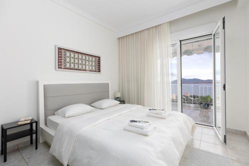 a white bedroom with a bed and a large window at Mimoza's Sea View Apartment in Paleo Tsifliki