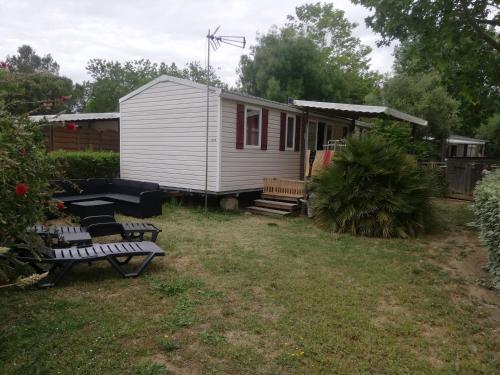 una pequeña casa blanca con dos bancos en el patio en Location Mobil Home, en Vias