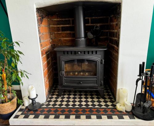 a stove in a brick fireplace with a checkered floor at Victorian quirky farm cottage next to forest & close to beach in Woodbridge