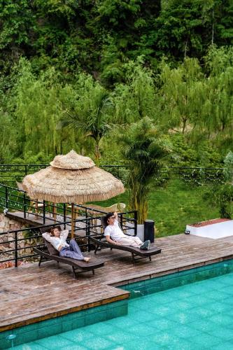 two people sitting in chairs under a straw umbrella next to a pool at Pandora Vista Retreat in Zhangjiajie