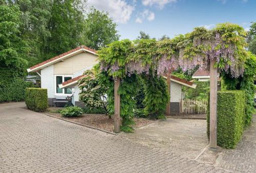 een huis met een pergola bedekt met planten bij Vlak aan het bos genieten van de rust & natuur. in Putten