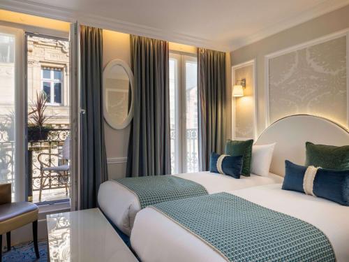 パリにあるホテル メルキュール ラ ソルボンヌ サンジェルマン デ プレのベッド2台とバルコニーが備わるホテルルームです。