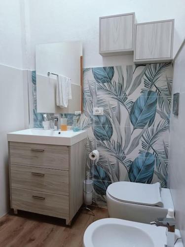 a bathroom with a toilet and a sink with a leafy wallpaper at Appartamento Luisa E in Villasimius