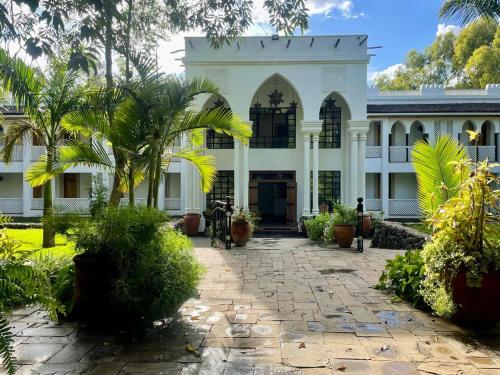 a white building with a palm tree in front of it at Small World Country Club in Athi River