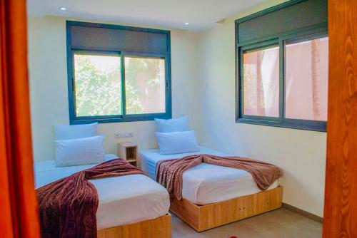 two beds in a room with two windows at Bungalow vert 1 in Essaouira