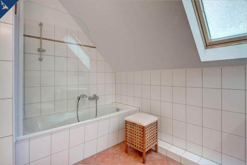 La salle de bains est pourvue de carrelage blanc, d'une baignoire et d'un tabouret. dans l'établissement Villen am See - 4-Raum Häuser DHH See- Idyll 2, à Korswandt