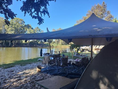 a tent with tables and chairs next to a lake at Worlds Apart - River Front Guest Farm & Camping in Bonnievale