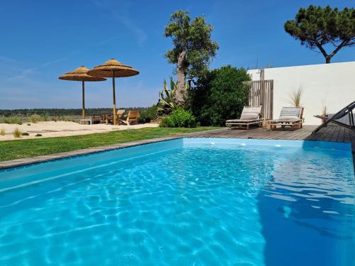 a blue swimming pool with two chairs and an umbrella at Casa Atlântico Carvalhal Comporta, apartamento piscina aquecida in Carvalhal