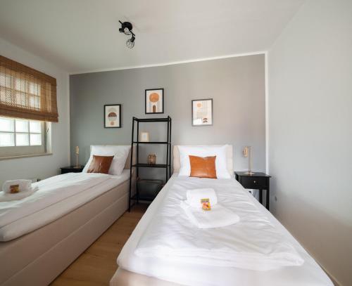 two beds in a room with white sheets and orange pillows at C4S -COME4STAY -InnHarmony- Stilvoll eingerichtetes Apartment für bis zu 8 Personen - Hochwertige Betten I voll ausgestattete Küche I Balkon I Badezimmer I WLAN I Smart TV in Töging am Inn