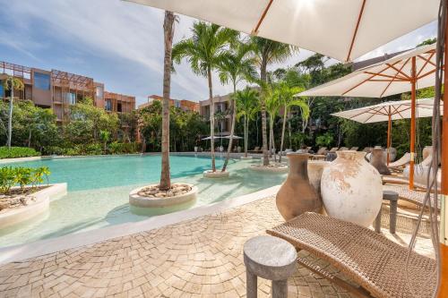 a pool with chairs and umbrellas next to a resort at Amazing 1BR Tulum Jungle with Restaurant, Pool and Gym in Tulum