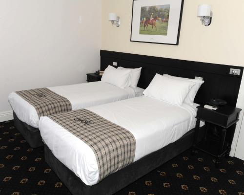 two beds in a hotel room with white sheets at The Yarrawonga Hotel in Yarrawonga