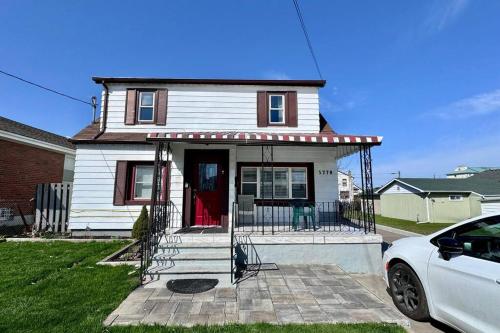 a small white house with a porch and a car at Near the Falls Two Bedroom - 5 min Walk to Clifton in Niagara Falls