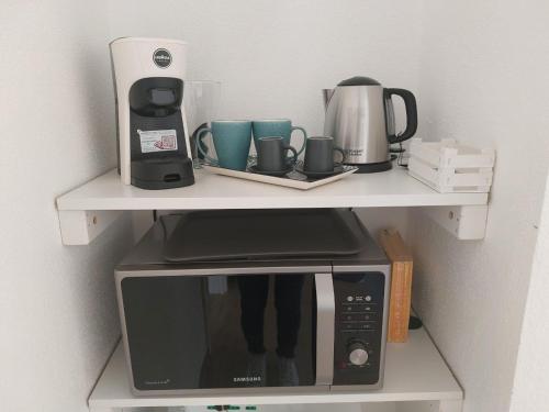 a white shelf with a microwave and cups on it at B&B Il Borgo delle Emozioni in Dolianova