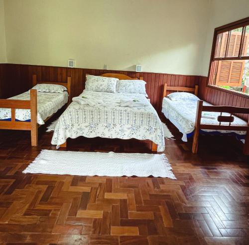 a bedroom with two beds and a wooden floor at Hotel Pião Mineiro in Monte Verde