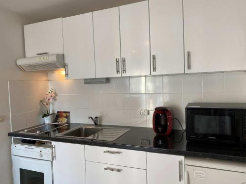une cuisine avec des armoires blanches, un évier et un micro-ondes dans l'établissement Appartement 2 pièces avec balcon, parking, proche plage et lac à Villers-sur-Mer - FR-1-712-81, à Villers-sur-Mer
