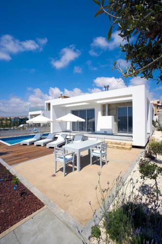 a white house with tables and chairs and a pool at Paradise Cove Luxurious Beach Villas in Paphos