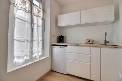 a kitchen with white cabinets and a window at Studio de standing en hypercentre proche Loire et parc in Châteauneuf-sur-Loire