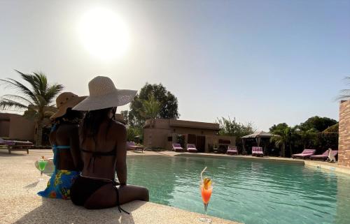 two women in bikinis sitting next to a swimming pool at Hôtel La Belle Etoile & SPA in Saly Portudal