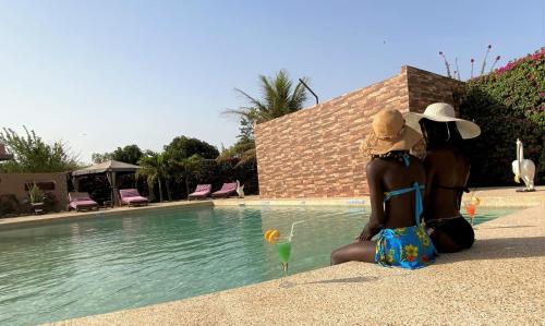 two women in bikinis sitting next to a swimming pool at Hôtel La Belle Etoile & SPA in Saly Portudal