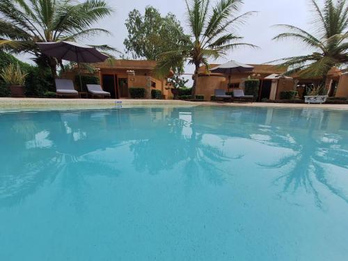 een groot blauw zwembad met palmbomen en parasols bij Hôtel La Belle Etoile & SPA in Saly Portudal