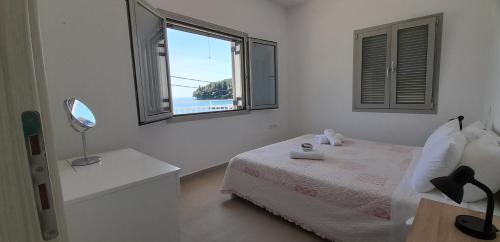 a white bedroom with a bed and a window at Villa Elsi upper apartment in Kalami