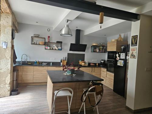 Il comprend une cuisine équipée d'un réfrigérateur noir et d'une table. dans l'établissement grande chambre confort les arcades, à Saint-Clar