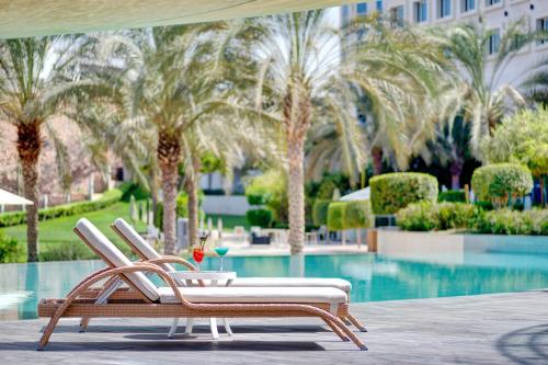 a pair of chairs sitting next to a pool with palm trees at Crowne Plaza Muscat OCEC, an IHG Hotel in Muscat