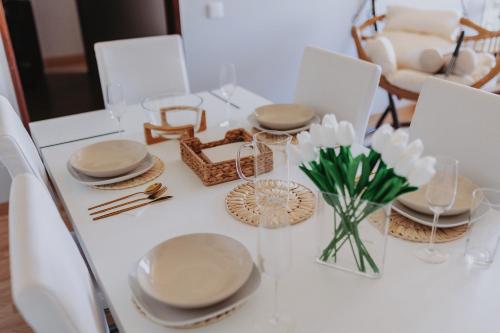 a white dining room table with plates and a vase of flowers at 3 bedroom apartment Cozy experience Lisbon in Mealhada