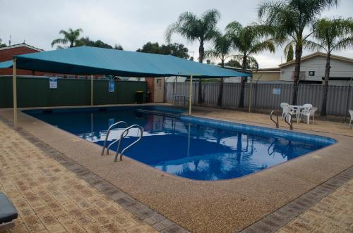a swimming pool with a blue umbrella and chairs at Acclaim Swan Valley Tourist Park in West Swan