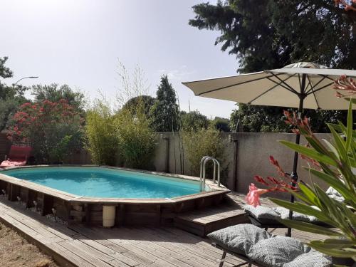 una piscina con sombrilla en una terraza de madera en Location saisonnière avec piscine et terrasse au pied du luberon, en Lauris