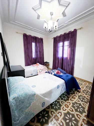 Habitación con 2 camas, cortinas moradas y lámpara de araña. en Entire House with private Rooftop en Alhucemas