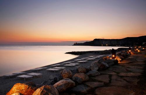 a beach with a row of chairs and the ocean at sunset at Portopiccolo Apartments in Sistiana