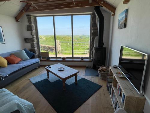 a living room with a couch and a table and a tv at Trengothal Barn in Porthcurno