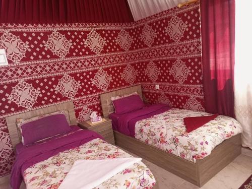 two beds in a bedroom with red and white wallpaper at Bedouin desert life camp& Jeep tours in Wadi Rum