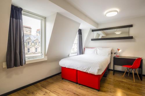 Schlafzimmer mit einem roten Bett, einem Schreibtisch und einem Fenster in der Unterkunft Tune Hotel Liverpool in Liverpool