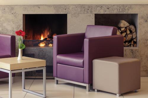 a living room with two purple chairs and a fireplace at Mercure Hotel Frankfurt Eschborn Ost in Eschborn