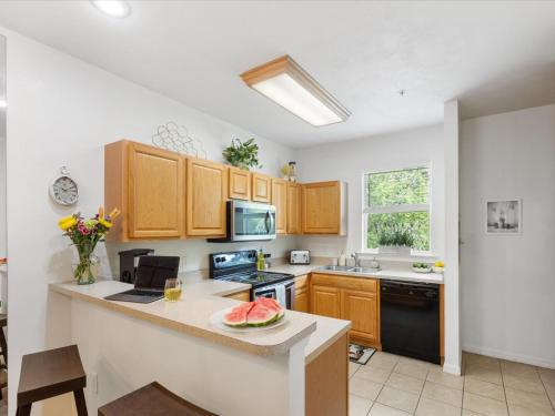 a kitchen with wooden cabinets and a counter top with a bowl of watermelon on at Convenient & Inviting - Fully-Equipped 2BD Condo in Gainesville