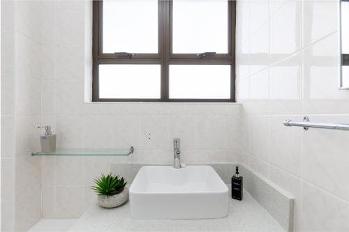 baño blanco con lavabo y ventana en La Corsica 15, Uvongo, en Margate