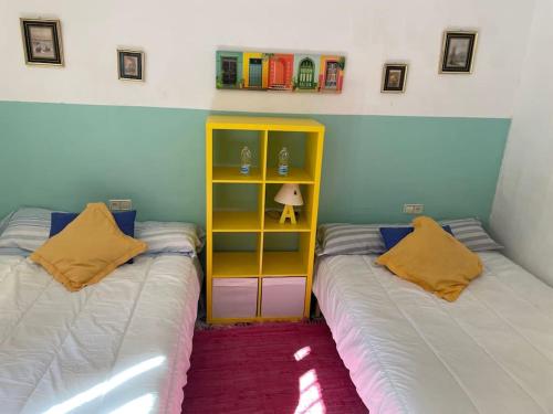 a bedroom with two beds and a yellow book shelf at Casa Rural Molera in Elda