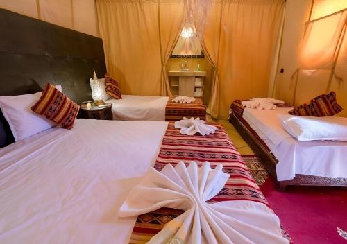 a hotel room with three beds with white sheets at Merzouga Top Desert Camp in Merzouga