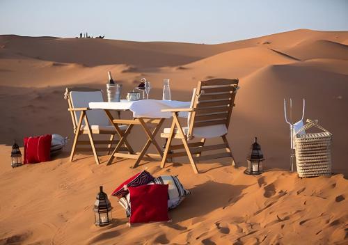 a table and chairs in the sand in the desert at Merzouga Lovely Luxury Camp in Merzouga