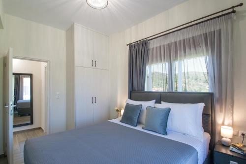 Un dormitorio con una cama con almohadas azules y una ventana en Ben’s Apartments, en Agia Paraskevi