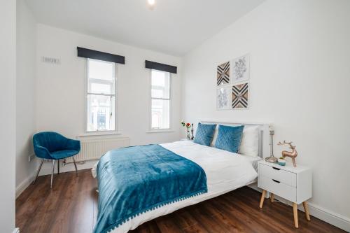 a white bedroom with a bed and a blue chair at Beautiful Flat Near the Center 11 min by tube in London