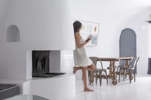 a woman in a white dress reading a book in a living room at Alta Vista Suites in Firostefani