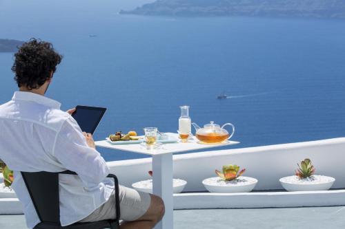 a man sitting on a balcony with a table with food at Alta Vista Suites in Firostefani