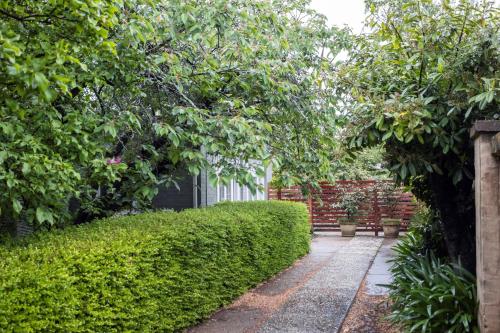 un jardin avec une haie et une passerelle dans l'établissement Silk Tree Studio - Steps to Cook Park, à Orange