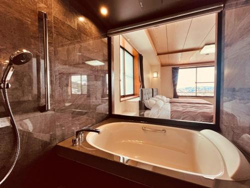 ein Bad mit einer Badewanne und einer Dusche mit einem Spiegel in der Unterkunft Hotel Omodaka in Yamanouchi