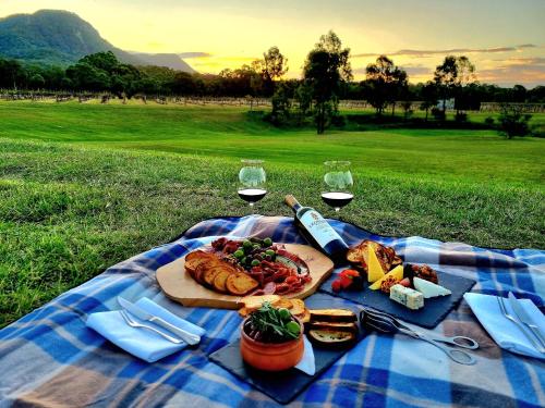 una coperta da picnic con un piatto di cibo e bicchieri di vino di Leogate Estate Villas a Pokolbin