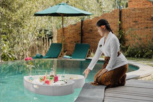 a woman sitting next to a table in a pool at Agastya Ubud Villa in Ubud